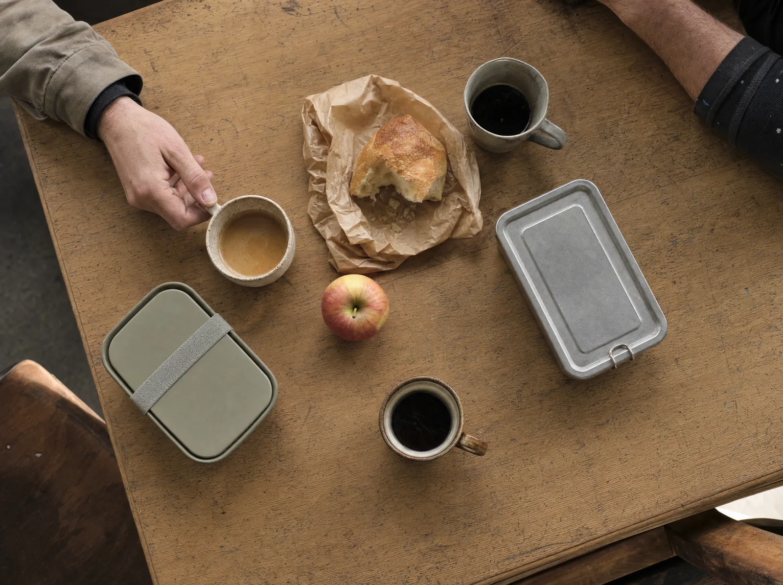 Kaffeetassen, Brot und Lunchboxen bei einer gemeinsamen Pause.