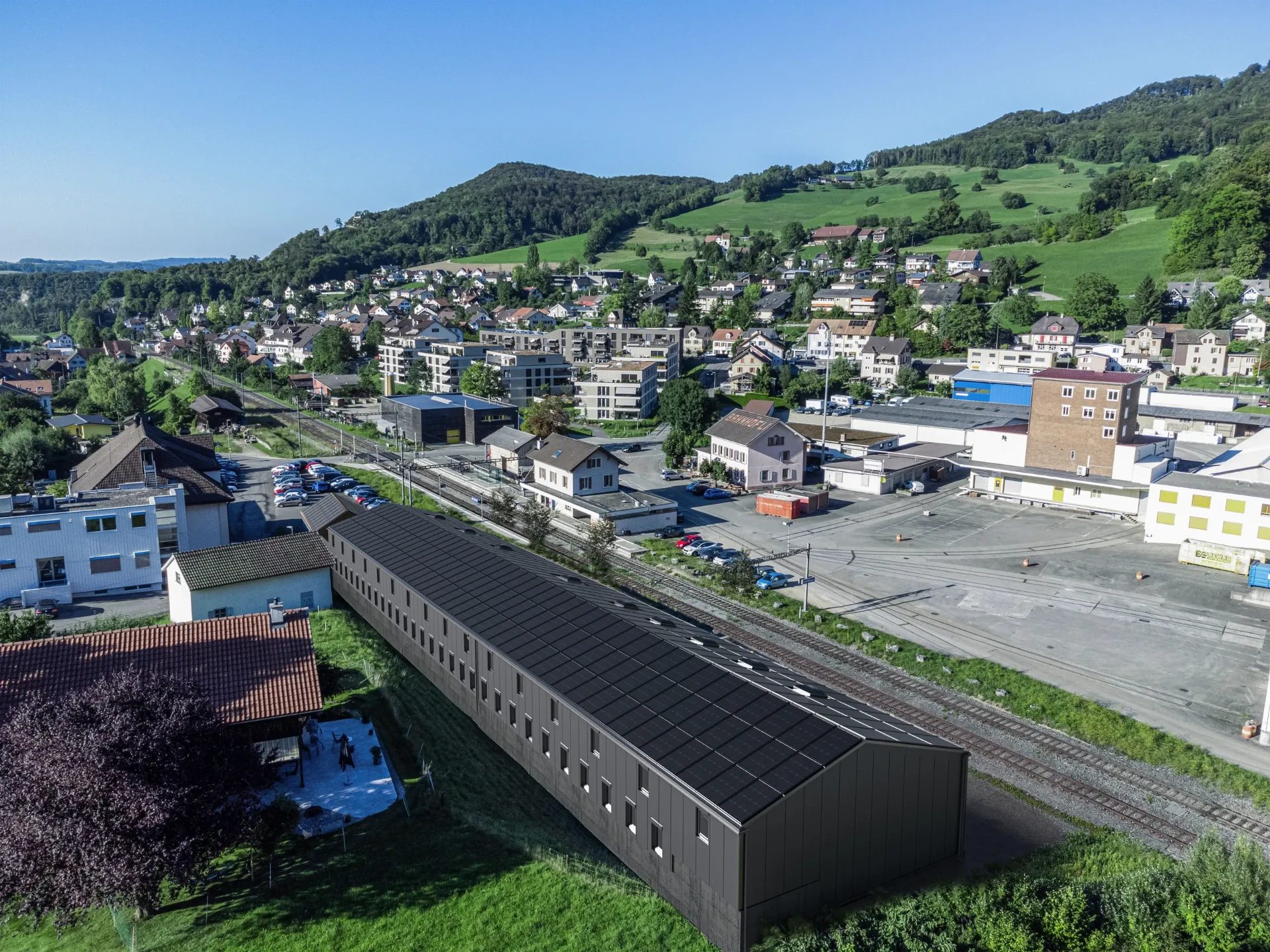 Das Areal aus der Luft mit Blick Richtung Dorf: die Langhalle mit Photovoltaik und Oberlichtern, dahinter der Bahnhof und der Ortskern von Läufelfingen