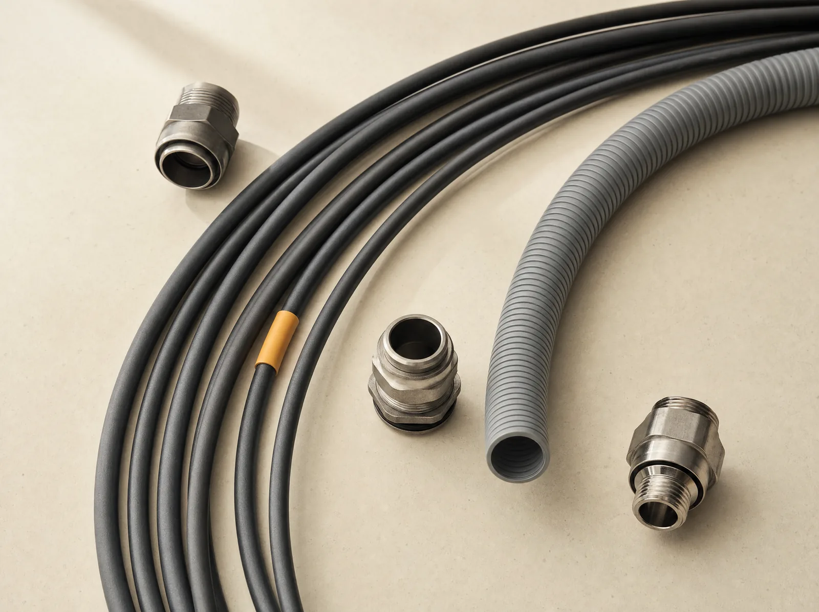 Kabel, flexibles Rohr und metallische Verbindungselemente auf einer hellen Fläche.