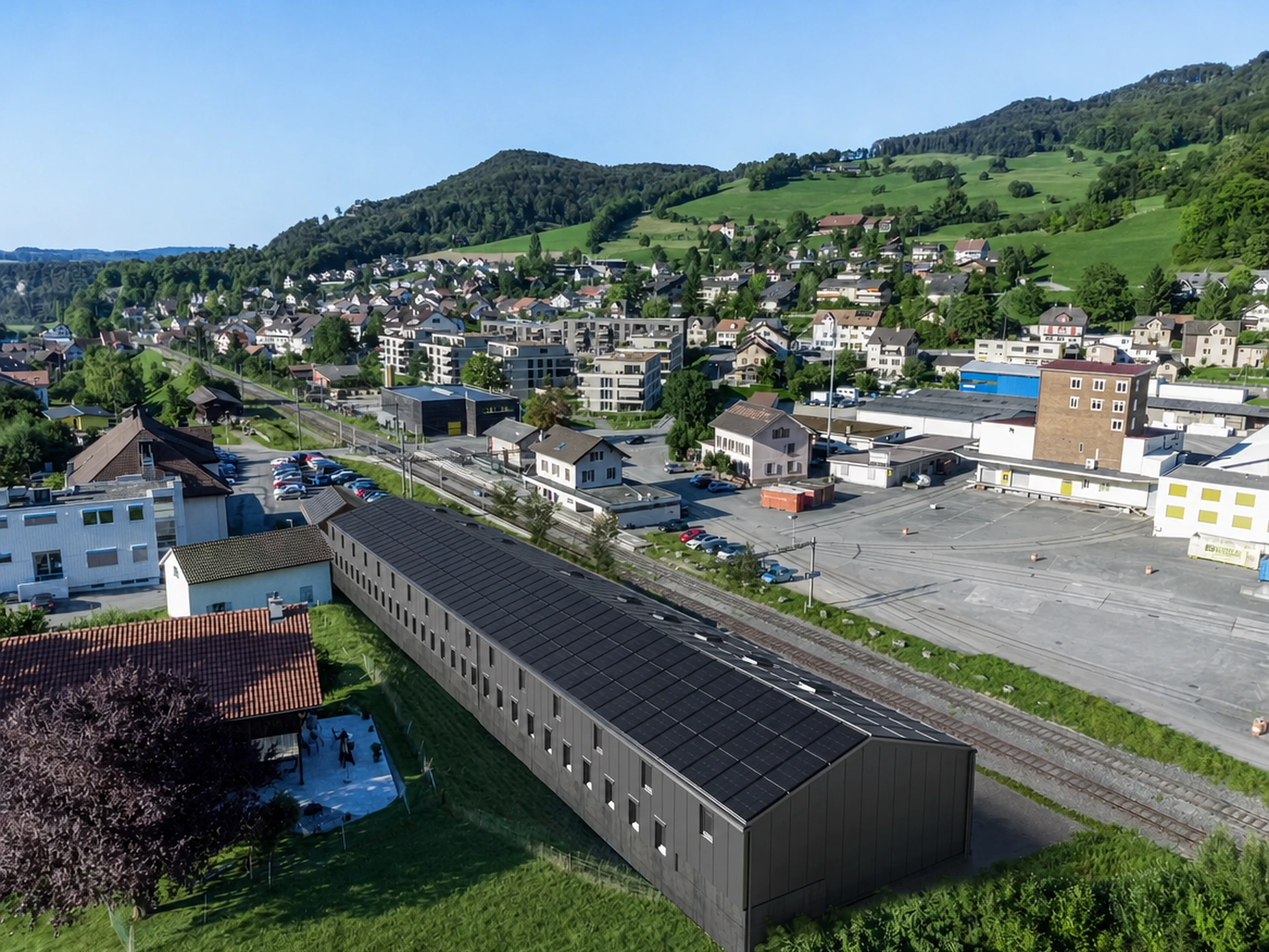 Das Areal aus der Luft mit Blick Richtung Dorf: die Langhalle mit Photovoltaik und Oberlichtern, dahinter der Bahnhof und der Ortskern von Läufelfingen